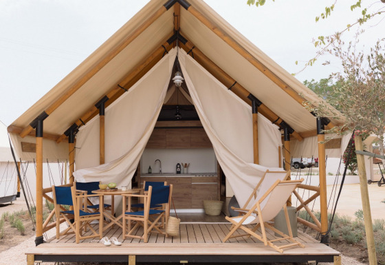 Safari tent Glamping Family Plus met houten terras, zitplaatsen, tafel en zichtbare keuken in natuurgebied.