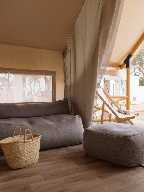 Binnenkant van een safaritent met gezellige zitplekken en mand bij Wecamp Cadaqués in Spanje, voor glamping.
