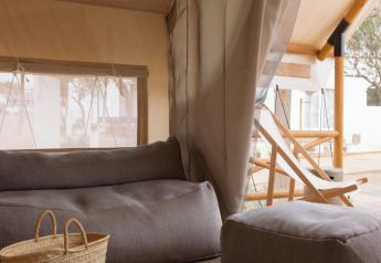 Vista interna di una tenda safari con sedute accoglienti e cestino da Wecamp Cadaqués, Spagna, per glamping.