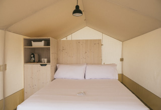 Interno di una tenda Cottage Family Tent presso Wecamp Cadaqués, Spagna, con letto matrimoniale e macchina da caffè.