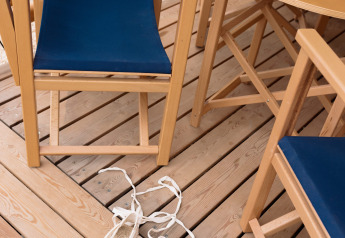 Terrazza in legno con sedie blu, tavolo con meloni e espadrillas bianche in tenda Glamping Comfort.