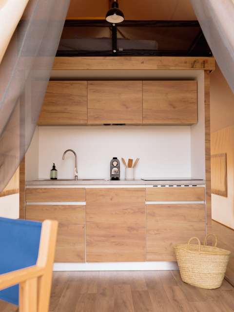 Binnenaanzicht van een knusse glampingkeuken met houten kasten in een safaritent bij Wecamp Cadaqués, Spanje.