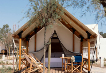 Tenda safari Glamping Couple con servizi igienici, veranda in legno, sedie a sdraio e alberi attorno.