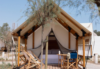 Tenda safari Glamping Couple con servizi igienici, veranda in legno, sedie a sdraio e alberi attorno.