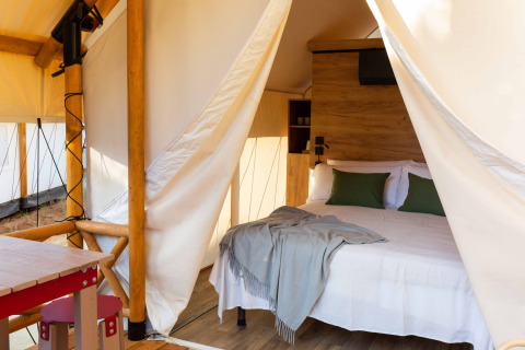 Safaritent bij Wecamp Cadaqués, Spanje, met een tweepersoonsbed, groene kussens, houten meubilair en sanitair.
