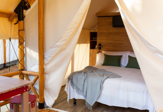 Safaritent bij Wecamp Cadaqués, Spanje, met een tweepersoonsbed, groene kussens, houten meubilair en sanitair.