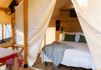 Tenda safari al Wecamp Cadaqués in Spagna con letto matrimoniale, cuscini verdi, mobili in legno e servizi privati.