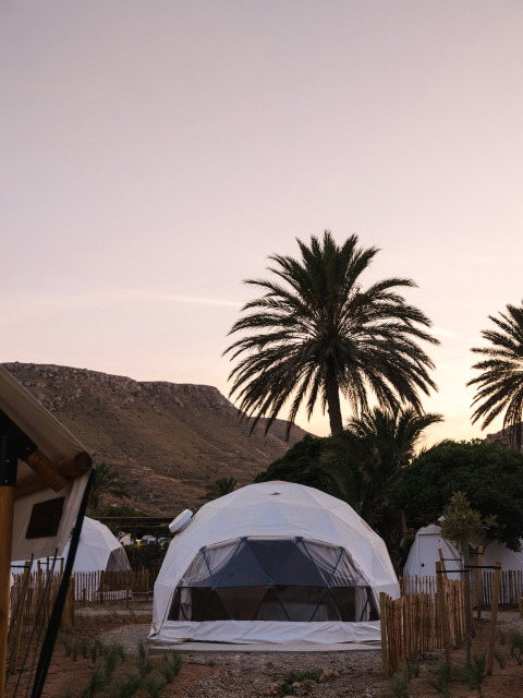 Cupole geodetiche e palme al tramonto nel villaggio vacanze Wecamp Cabo de Gata, Andalusia, Spagna.