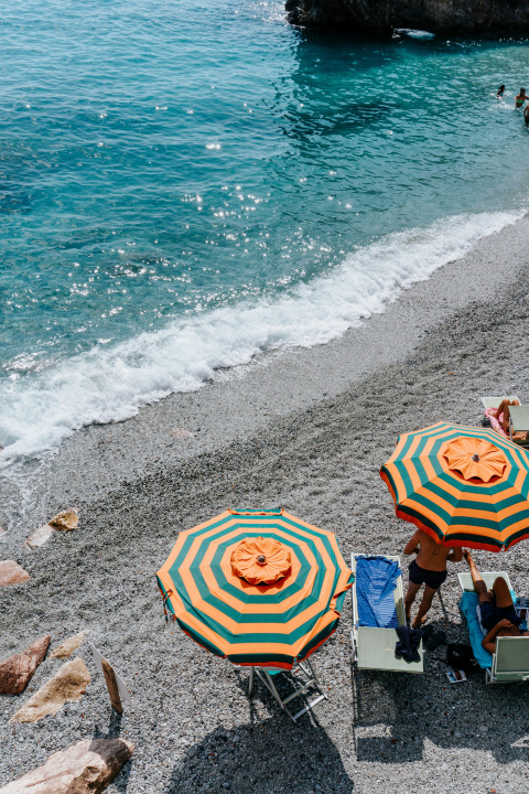 Strandscene ved Castagneto Carducci med to farverige parasoller, solstole og klart blåt vand i Toscana.
