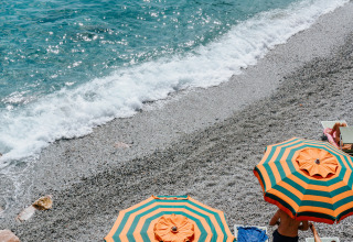 Strandscene ved Castagneto Carducci med to farverige parasoller, solstole og klart blåt vand i Toscana.