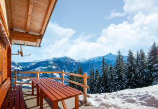 Udsigt fra Almhütte Nase chalet i Østrig med træbænk og sneklædte bjerge i baggrunden.