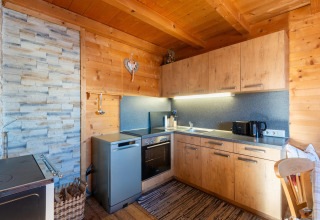 Moderne alpehytte køkken med trævægge, grå apparater og hyggelig belysning på 'Almhütte Nase' i Østrig.