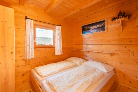 Et hyggeligt soveværelse i Almhütte Nase-chalet i Østrig med trævægge, dobbeltseng og vindue.