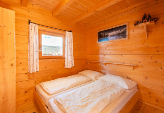 Et hyggeligt soveværelse i Almhütte Nase-chalet i Østrig med trævægge, dobbeltseng og vindue.