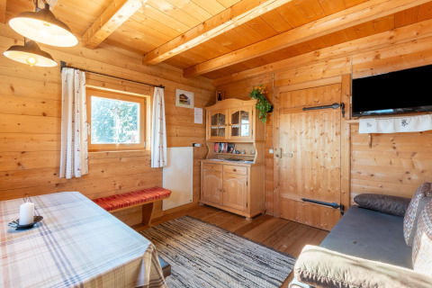 Hyggelig stue i træ med spisebord, bænk, kommode og vindue, i Almhütte Nase-chalet i Østrig.