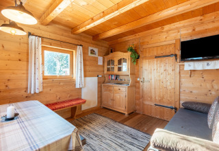 Hyggelig stue i træ med spisebord, bænk, kommode og vindue, i Almhütte Nase-chalet i Østrig.
