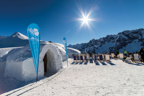 Solbeskinnet vinterscene ved Almhütte Nase i Østrig med iglo, stole og sneklædte bjerge.