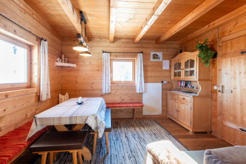 Hyggelig spisestue i træ med vinduer, træbord, bænke og skænk på en bjælkehytte kaldet Almhütte Nase i Østrig.