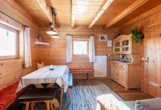Hyggelig spisestue i træ med vinduer, træbord, bænke og skænk på en bjælkehytte kaldet Almhütte Nase i Østrig.