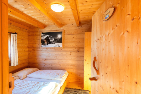 Hyggeligt værelse i træ på 'Almhütte Nase' chalet i Østrig med dobbeltseng og bjergfoto på væggen.