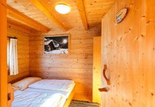 Hyggeligt værelse i træ på 'Almhütte Nase' chalet i Østrig med dobbeltseng og bjergfoto på væggen.
