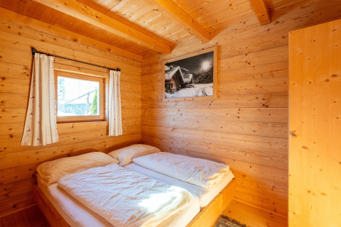 Hyggeligt soveværelse i træ med dobbeltseng, lille vindue og vægkunst på Almhütte Nase, Østrig.