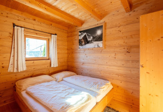 Hyggeligt soveværelse i træ med dobbeltseng, lille vindue og vægkunst på Almhütte Nase, Østrig.