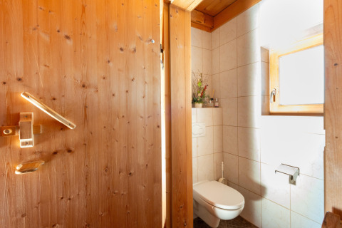 Hyggeligt badeværelse med trægulv og vægge, væghængt toilet og vindue i Almhütte Nase, Østrig.