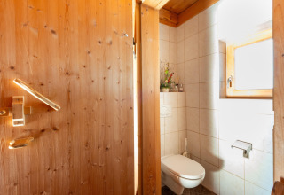 Hyggeligt badeværelse med trægulv og vægge, væghængt toilet og vindue i Almhütte Nase, Østrig.