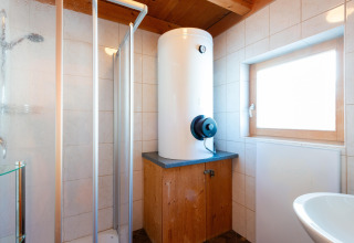 Moderne badeværelse med varmtvandsbeholder, brusekabine og vindue på Almhütte Nase i Østrig.