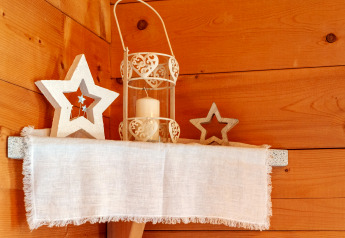 Estante de madera en Almhütte Nase, Austria, decorado con estrellas, vela y tela blanca sobre pared de madera.
