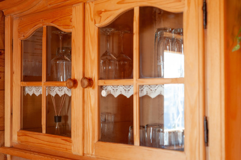 Træskab med glaslåger i Almhütte Nase, Østrig, viser glas og dekorativt blonder på hylden.