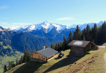 Chalet Almhütte Nase en Austria con montañas nevadas, bosques y valles bajo un cielo despejado.