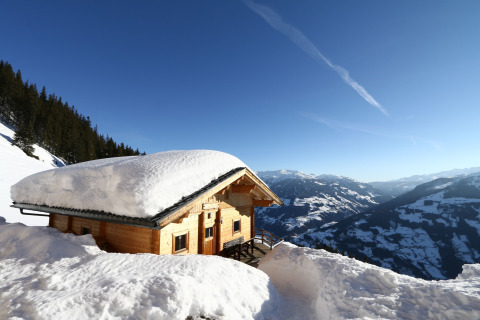 Almhütte Nase chalet med tykt snelag på taget, beliggende i sneklædte bjerge i Østrig under blå himmel.