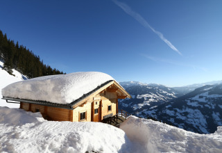 Almhütte Nase chalet med tykt snelag på taget, beliggende i sneklædte bjerge i Østrig under blå himmel.