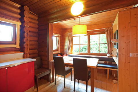 Cozy dining area inside a wooden chalet with large windows, natural light, and modern furnishings in Austria.