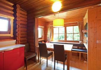 Cozy dining area inside a wooden chalet with large windows, natural light, and modern furnishings in Austria.
