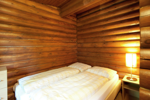 Bedroom in Chalet Catharina im Brixental, Austria, with wooden log walls, double bed, and bedside lamp.