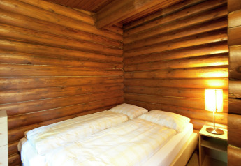 Bedroom in Chalet Catharina im Brixental, Austria, with wooden log walls, double bed, and bedside lamp.