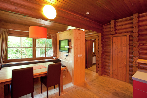 Wooden interior of an Austrian chalet with a dining table, TV, and large windows overlooking nature.