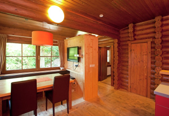 Wooden interior of an Austrian chalet with a dining table, TV, and large windows overlooking nature.