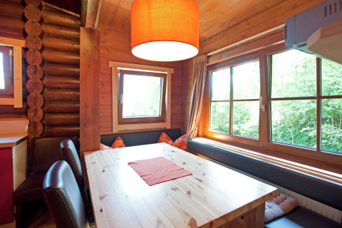 Dining nook in Chalet Catharina, Austria with a wooden table, bench seating, large windows and cushions.