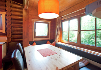 Dining nook in Chalet Catharina, Austria with a wooden table, bench seating, large windows and cushions.