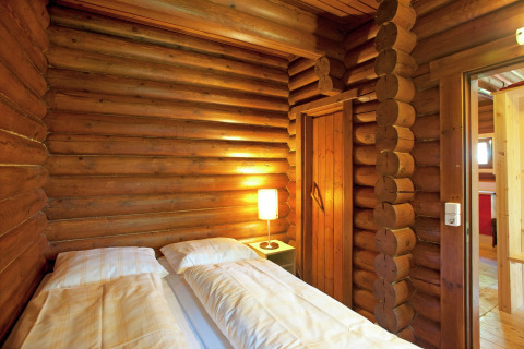 Cozy wooden log cabin room with double bed and warm lamp at Chalet Catharina im Brixental, Austria.