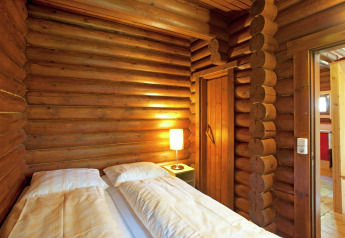 Cozy wooden log cabin room with double bed and warm lamp at Chalet Catharina im Brixental, Austria.