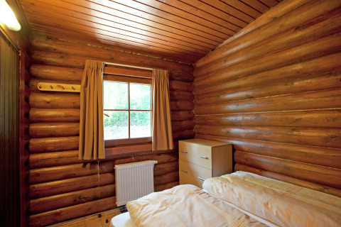 Cozy log cabin bedroom at Chalet Catharina with bed, window, curtains, radiator, and wooden chest.