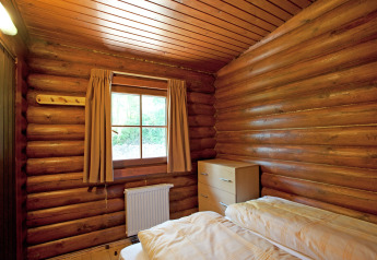 Cozy log cabin bedroom at Chalet Catharina with bed, window, curtains, radiator, and wooden chest.