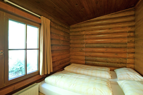Cozy bedroom with wooden log walls, double bed, and large window in Chalet Catharina im Brixental, Austria.