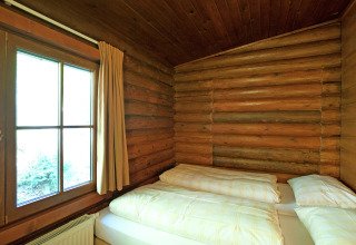 Cozy bedroom with wooden log walls, double bed, and large window in Chalet Catharina im Brixental, Austria.