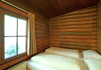 Cozy bedroom with wooden log walls, double bed, and large window in Chalet Catharina im Brixental, Austria.